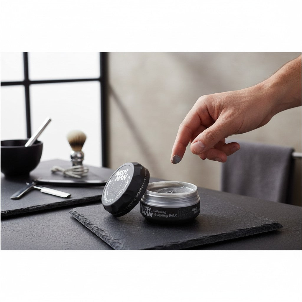 cosmetigo.be Nishman C2 Grey Smoked styling wax met sterke hold en tijdelijke grijze kleuring. Een hand pakt wat wax uit de pot.